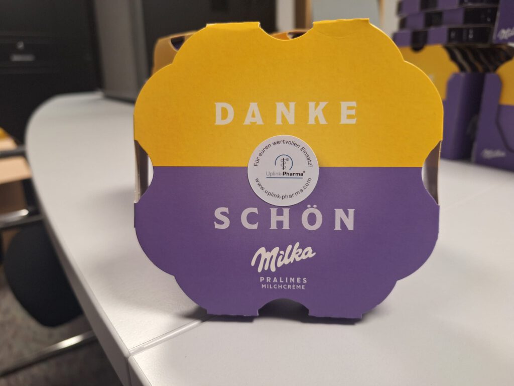 Einzelne Milka-Dankespralinen-Packung mit Uplink-Pharma-Sticker als Teil der 700 Dankesgeschenke für das Kreiskrankenhaus Weilburg.